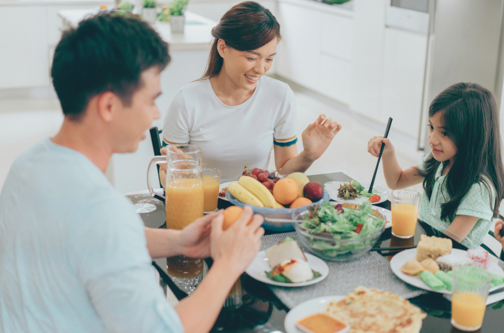 A young mother and father share breakfast at the table with their school-aged daughter.