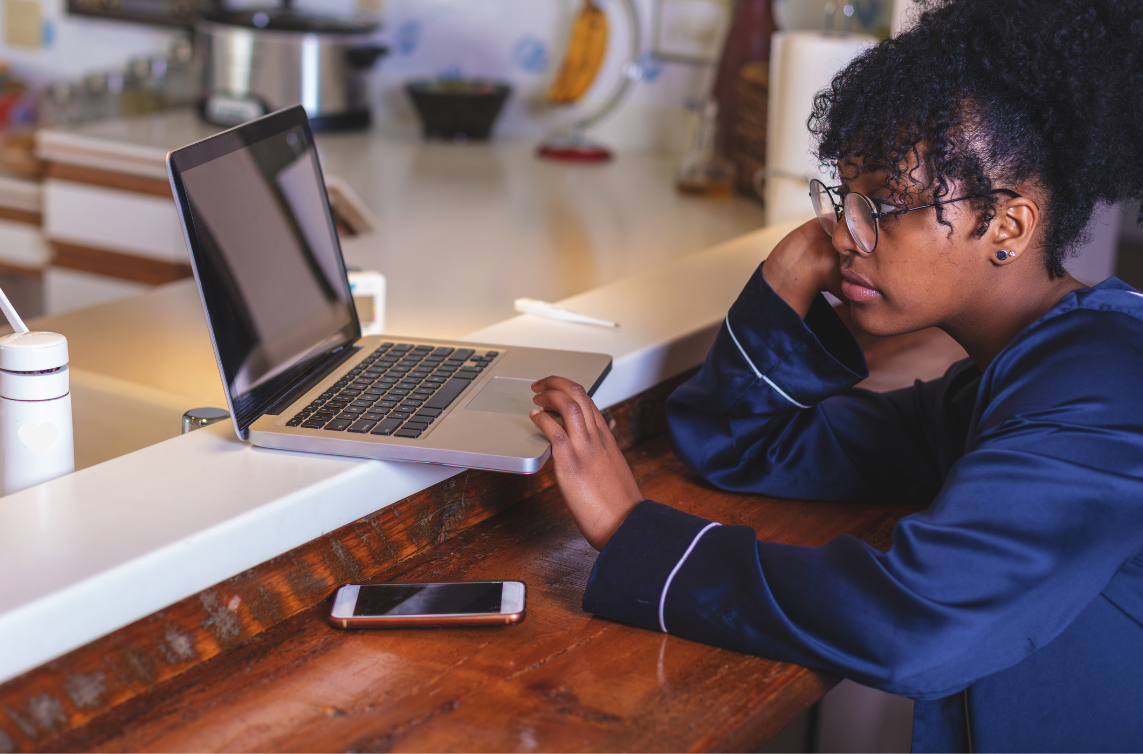 woman with glasses sitting at her kitchen counter looking at her Macbook laptop