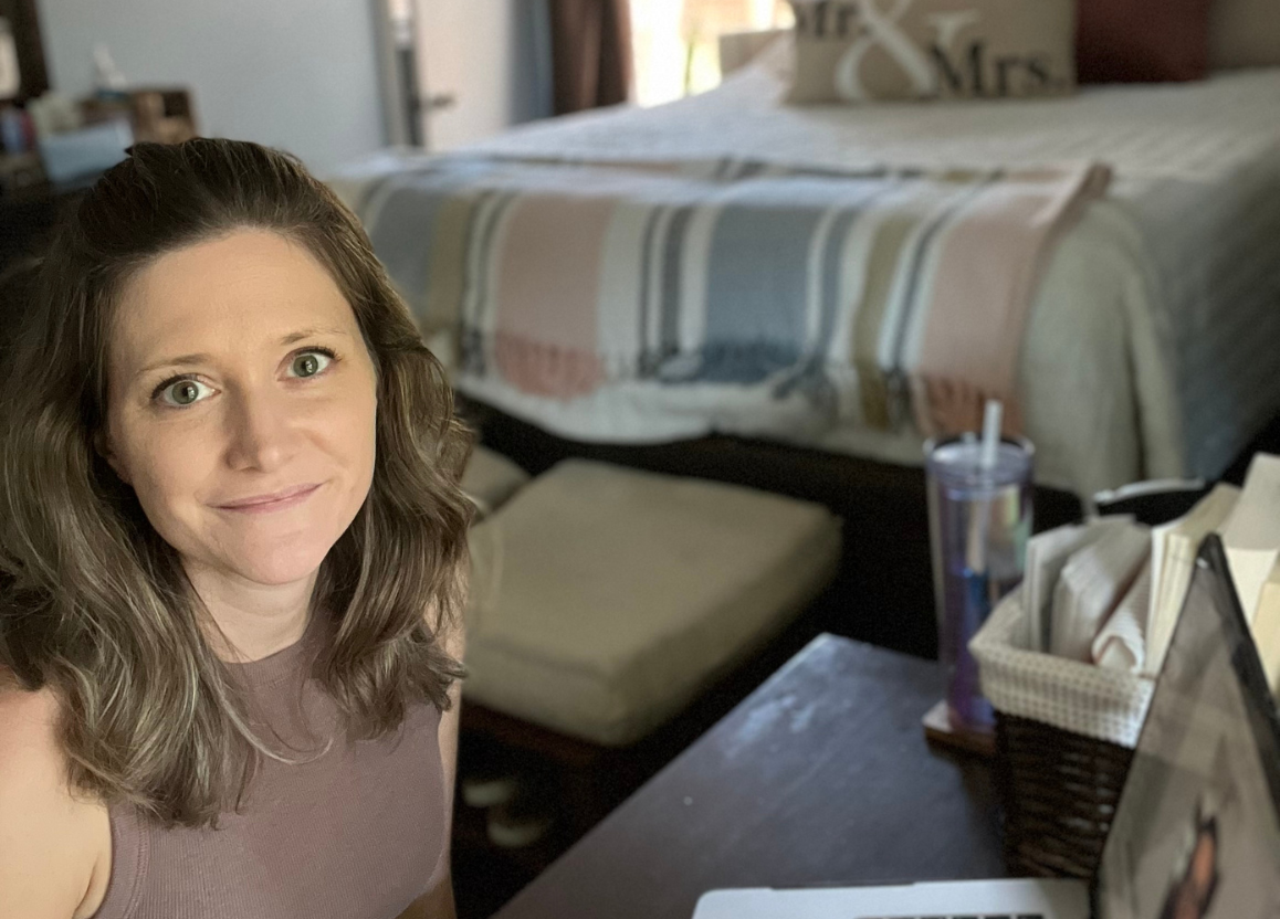 woman (Madison, dietitian counselor) softly smiling up at camera sitting in front of laptop