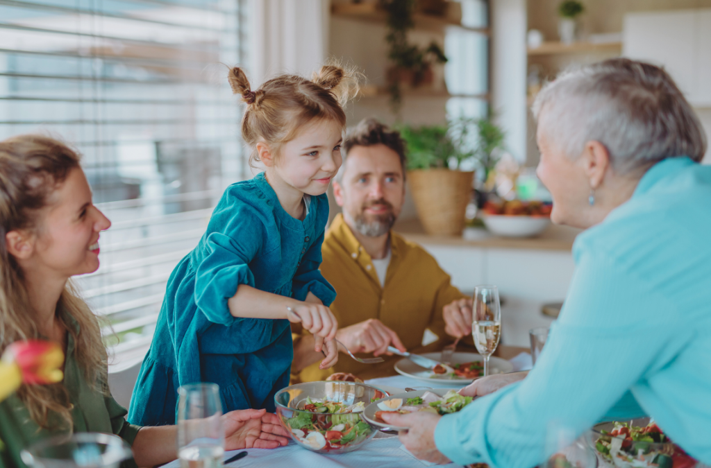 a grandma helping hold a young girl's plate while the girl scoops some salad onto the plate, both are smiling
