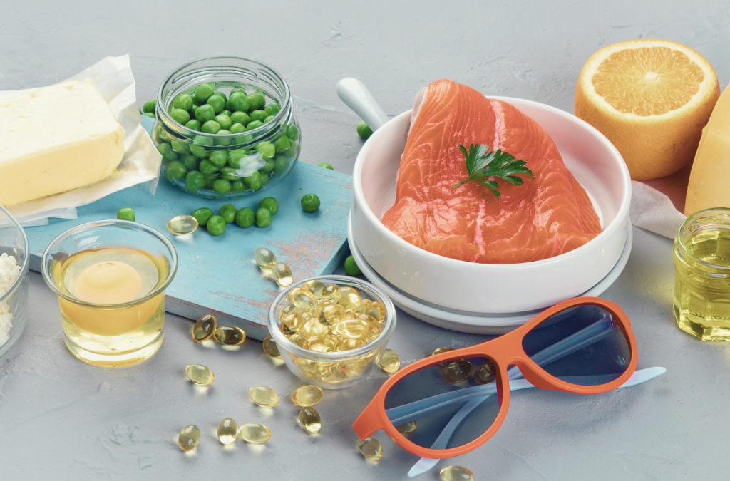 table with vitamin d-containing foods like peas, eggs, and salmon as well as a cup of supplements and a pair of sunglasses