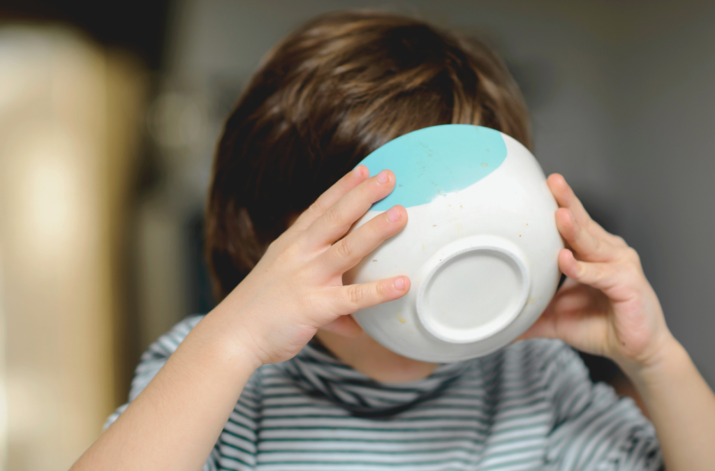 child holding a bowl covering his face in order to drink everything out of it