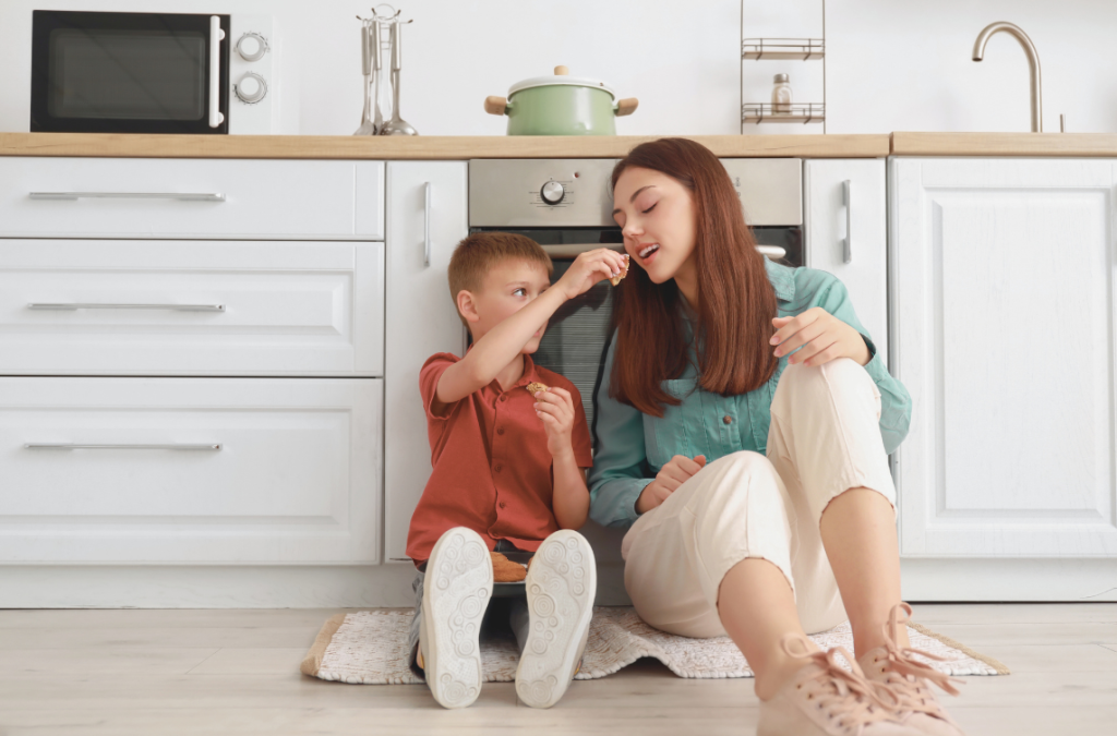 child and parent looking content sitting on kitchen floor while the child feeds parent a bite of food