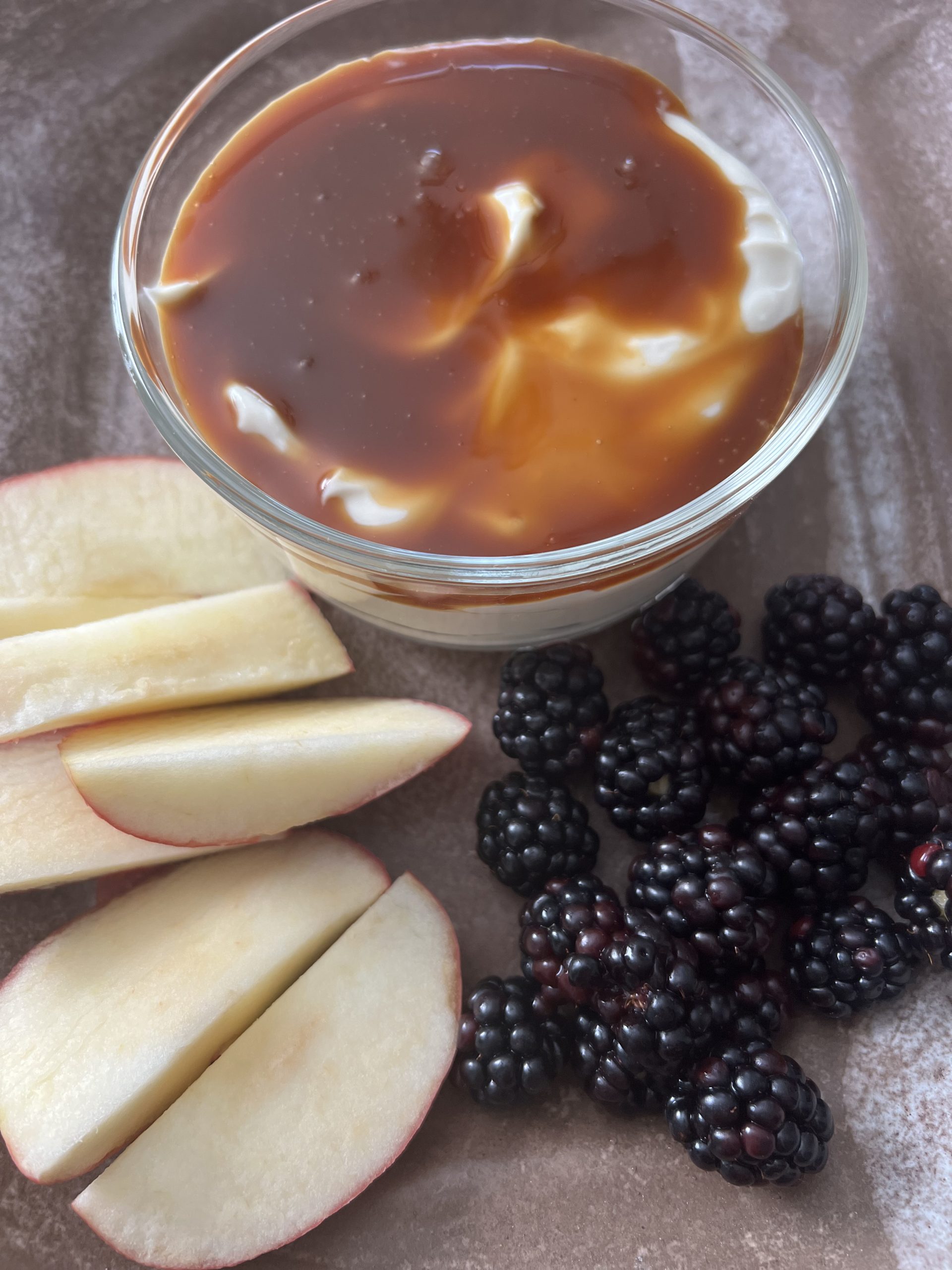 creamy greek yogurt dip with caramel on a plate with apple slices and blackberries